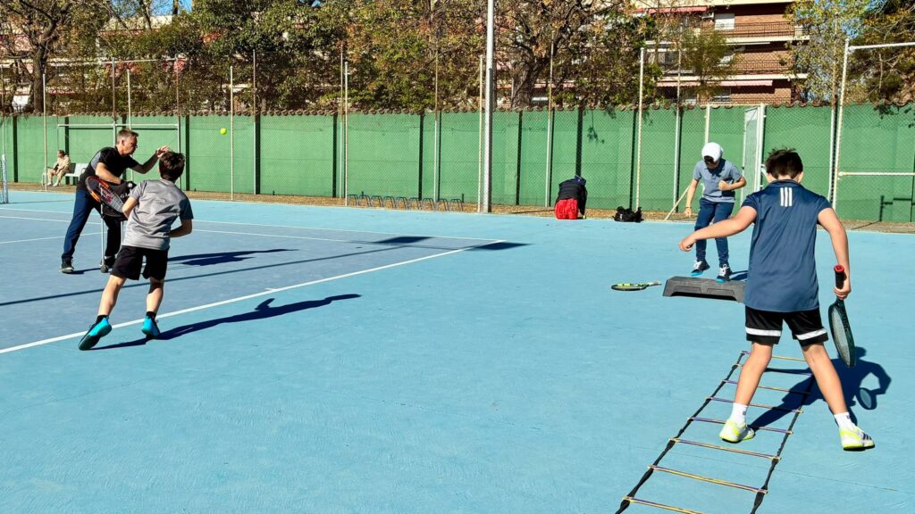 Imagen durante una clase en Fair Play Élite en un ejercicio con estaciones donde un niño golpea, otro hace un ejercicio de escalera y el otro hace salto sobre banco